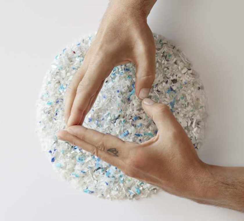 Hands formed in a heart shape above granulate from recycled plastic packaging by ALPLA Group