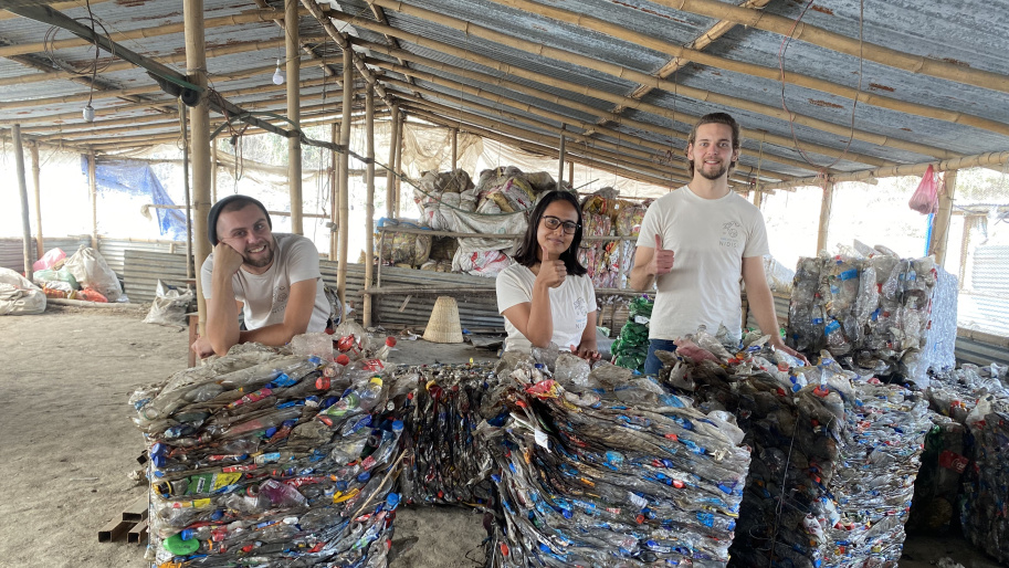 ALPLA employees and partners standing behind compressed bales of collected plastic waste at a recycling site, supporting community engagement and responsible resource management.